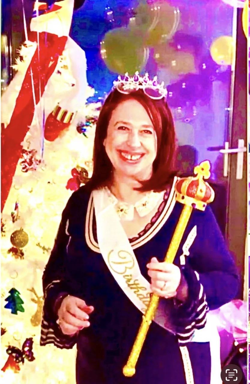 Улыбающаяся женщина в тиаре и с лентой на праздничном фоне с шарами и украшенным деревом